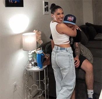  Smiling woman in white top and jeans hugging a man sitting on a couch in a cozy living room