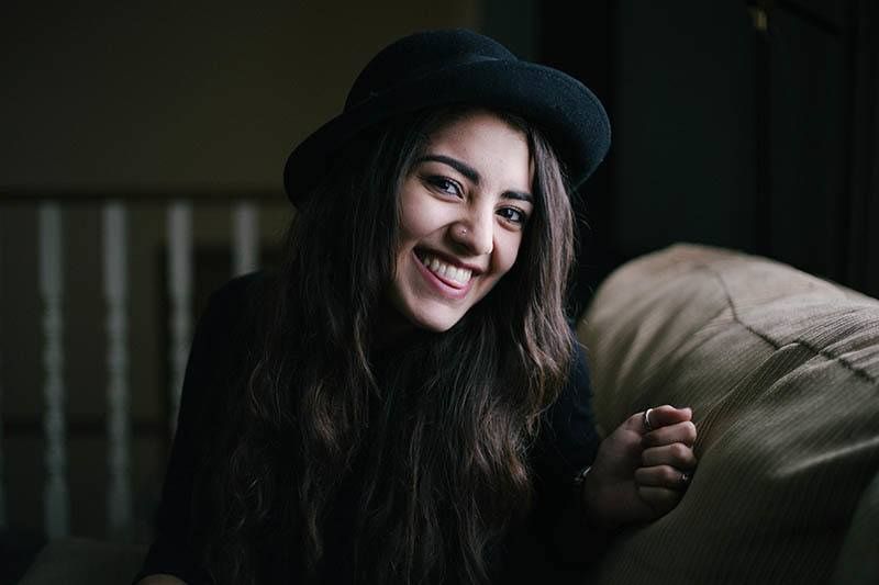  Smiling woman with long hair and black hat sitting on a couch indoors